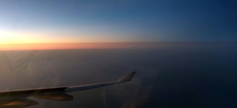 Airplane wing amidst setting sun creating hues of yellow and red in horizon seen from the window of the airplane