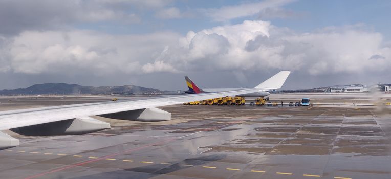 Airplane wing covered in snow and ice in docking bay in a mountain region with clouds in the background