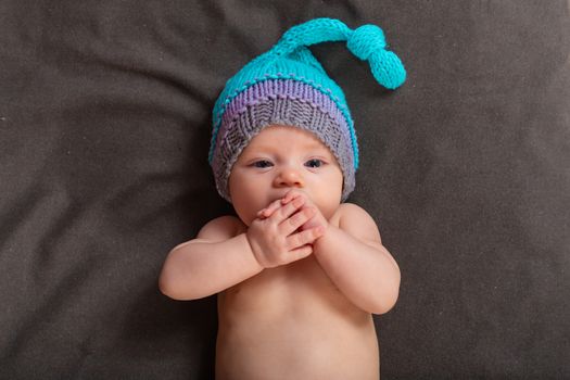 Beautiful baby girl in the studio on a dark gray background in bare pants and a winter hat.