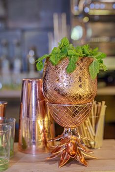 Gold metallic cup with mint and shaker in the background on bar