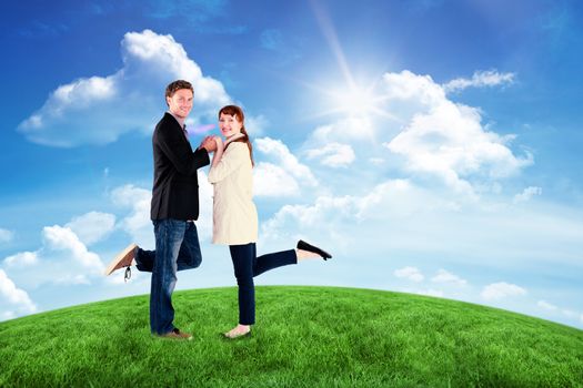 Smiling couple with raised legs against green hill under blue sky
