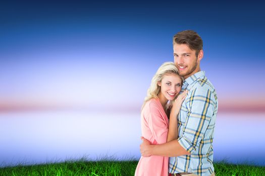 Attractive couple embracing and smiling at camera against green grass under blue and purple sky