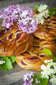 Homemade yeast pie with jam on a wooden table with spring lilac and white flowers. Vertical image
