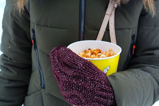 Young woman holding popcorn in winter, in mittens	