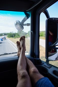The male passenger put his feet on the front panel in the cab of the truck. Hairy legs.