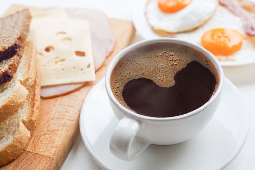 Breakfast with coffee, toasted bread, eggs, bacon, cold cuts and cheese on table