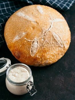 Sourdoug starter and wheat sourdough bread. Wheat sour dough starter in glass jar and homemade round sourdough bread on black background, copy space. Home made sourdough bread making concept Vertical.