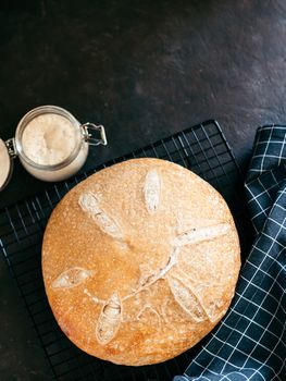 Wheat round sourdough bread and sourdoug starter in glass jar. Top view of delicious homemade sourdough bread on black background with copy space. Home made sourdough bread making concept. Vertical.