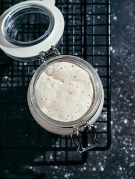 Wheat sourdough starter. Glass jar with sourdough starter on dark background, copy space. Vertical.