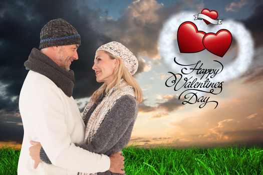 Happy couple in winter fashion embracing against green grass under blue and orange sky