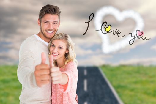 Attractive couple showing thumbs up to camera against road on grass