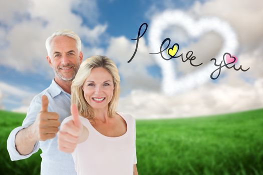 Smiling couple showing thumbs up together against green field under blue sky
