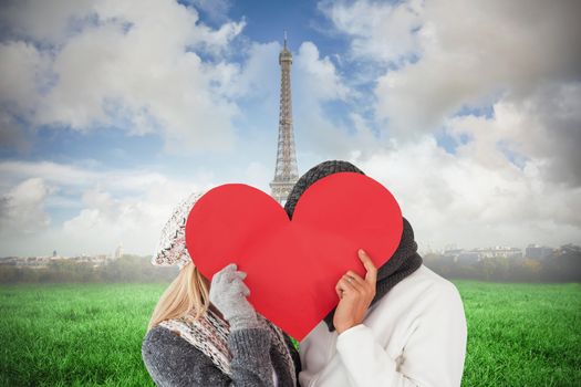 Couple in winter fashion posing with heart shape against eiffel tower