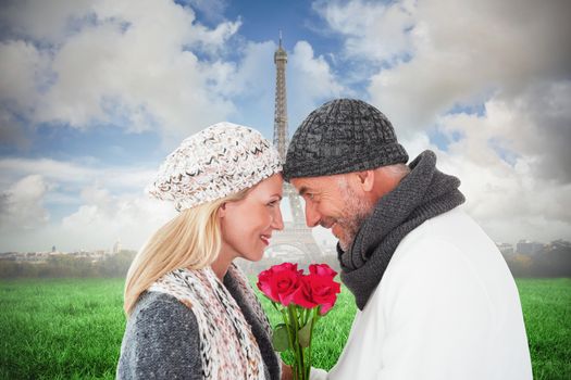 Smiling couple in winter fashion posing with roses against eiffel tower