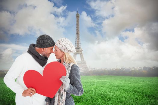 Smiling couple in winter fashion posing with heart shape against eiffel tower