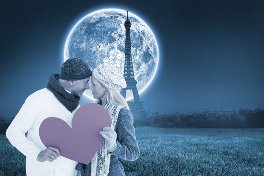 Smiling couple in winter fashion posing with heart shape against large moon over paris