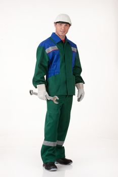 Young man in the uniform on isolated background holding a big wrench