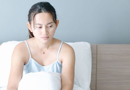 Closeup woman sitting on bed in the bedroom with thinking or depressed feeling, selective focus