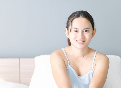 Close up asian woman smiling with happy face lying on white bed in the morning, selective focus