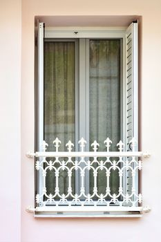 Modern metal-plastic transparent balcony window doors with lattice shutters with metal decorative figured lattice of the balcony, framed in the Greek style.