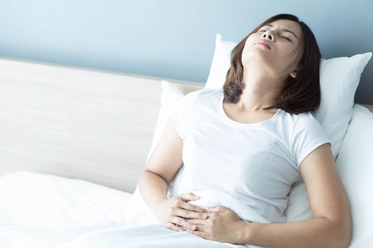 Close up woman stomachache lying on white bed, health care concept, selective focus