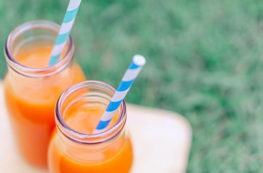 Closeup top view glass of carrot juice with green grass background, selective focus