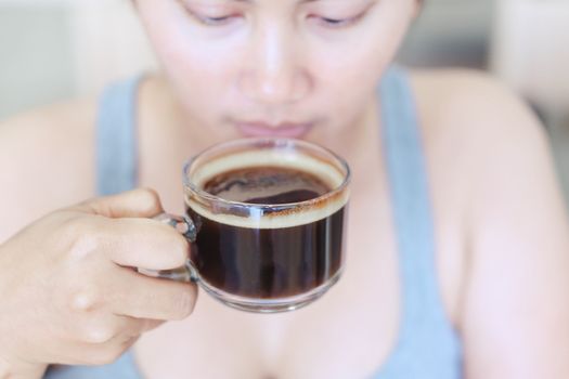 Closeup woman hand holding glass of hot americano coffee, selective focus, vintage tone