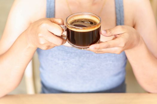 Closeup woman hand holding glass of hot americano coffee, selective focus, vintage tone