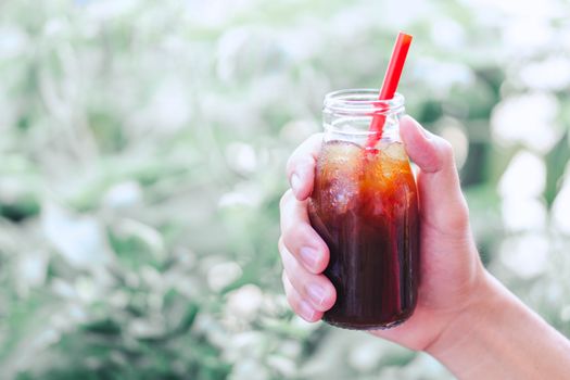 Close up hand holding bottle glass of americano coffee with green nature background, vintage tone