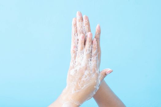 Closeup woman's hand washing with soap on blue background, health care concept