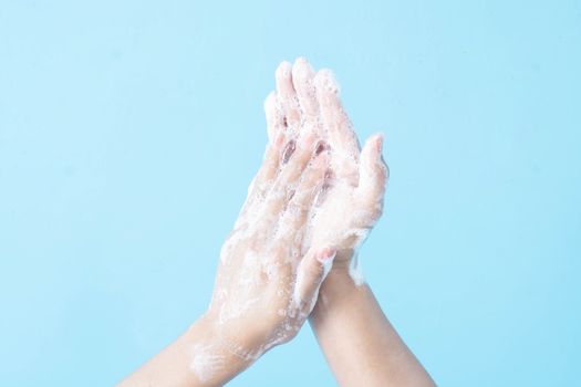 Closeup woman's hand washing with soap on blue background, health care concept