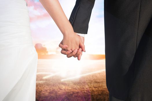 Close up of cute young newlyweds holding their hands against field with light wave