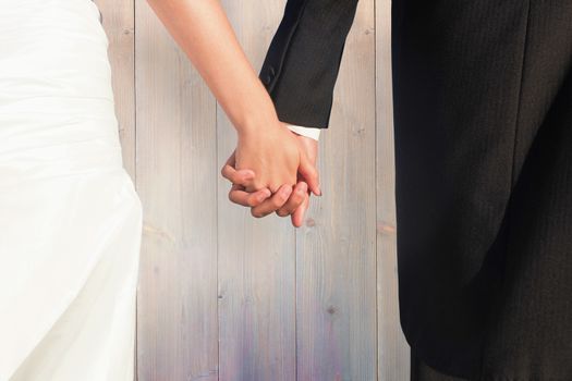 Close up of cute young newlyweds holding their hands against pale grey wooden planks