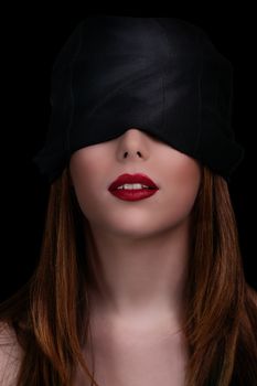 Low key shot of a gorgeous young woman with a black blindfold covering her eyes, isolated on black background. Beautiful blindfolded woman with red lipstick. 