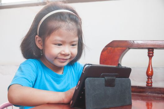 Asian Girl learning online course or playing game online on Digital Wireless Device or Tablet at home as Technology e-learning concept.
