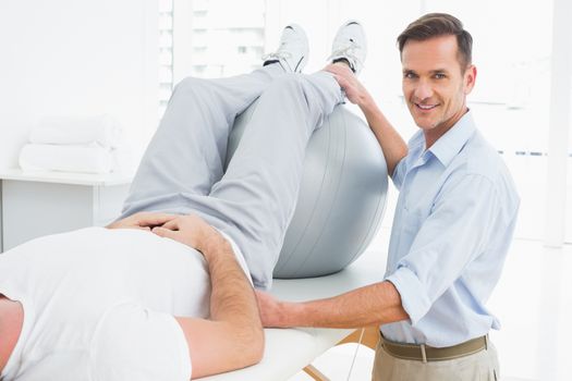 Physical therapist assisting young man with yoga ball in the gym at hospital