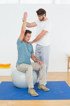 Young man sitting on yoga ball while working with a physical therapist