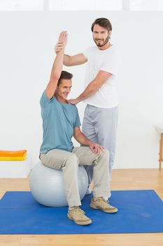 Young man sitting on yoga ball while working with a physical therapist