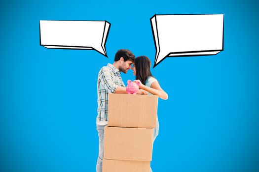 Happy young couple with moving boxes and piggy bank against blue background with vignette