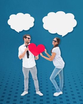 Hipster couple smiling at camera holding a heart against blue