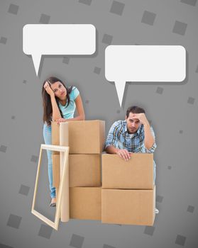 Stressed young couple with moving boxes against grey
