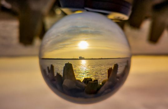 Sunset over baltic sea and coast of Swinoujscie city seen from breakwater in crystal glassball reflection