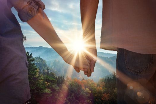 Couple holding hands in park against sunrise over mountains