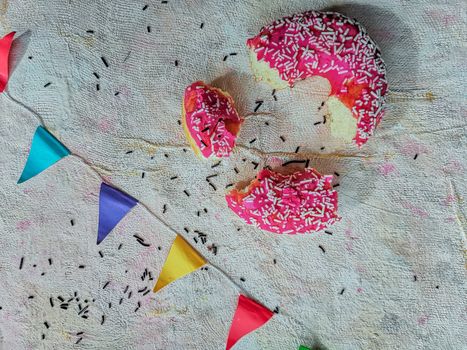 Flat lay of fragments of pink donut with colorful triangles on light fabric background