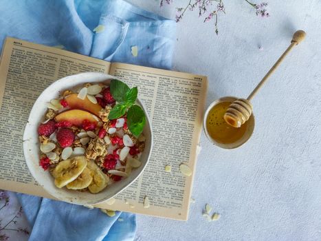 Morning Flat lay of bowl with fruity muesli on book and ramekin with honey