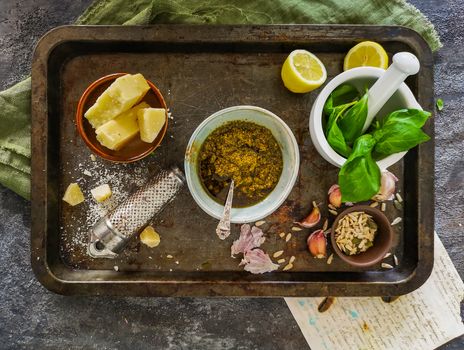 Green pesto, basil in mortar, parmesan cheese, garlic on metal tray