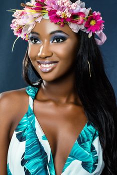 Close up studio beauty portrait of young african woman wearing flower garland.Young girl with long hair and charming smile against dark blue background. 