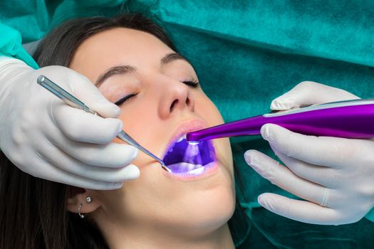 Macro close up of hand working on female teeth with blue led curing light.