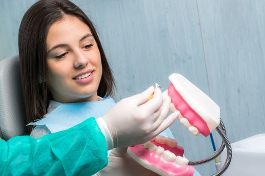 Close up of hand showing dental patient interdental cleaning on oversize human teeth prosthesis. Young woman in clinic.