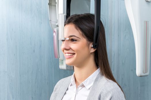 Close up portrait of young female dental patient standing in digital cephalometric panorama x-ray machine.